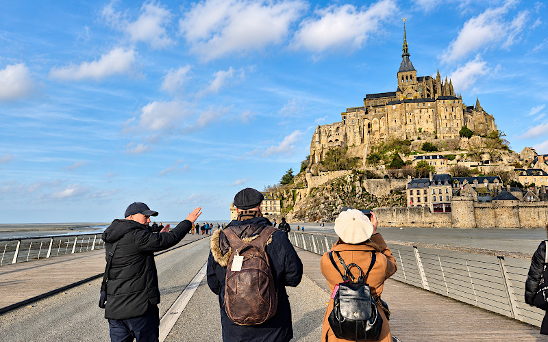 Grupo de turistas en la pasarela del Mont-Saint-Michel con la abad�a al fondo bajo un cielo azul