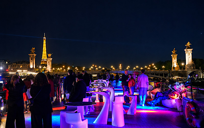 Velada privada en la cubierta de un barco en el Sena, con vistas a la Torre Eiffel iluminada y el puente Alejandro III